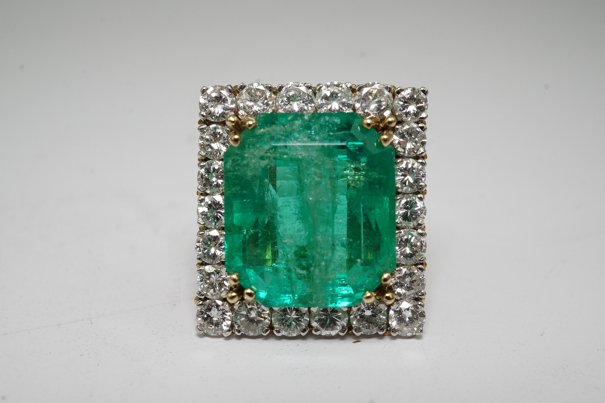 A Stern 18ct white and yellow gold, emerald and diamond dress ring, the central green emerald cut emerald approximately 8.0ct and surrounded by twenty two circular cut diamonds, approximately 2.7ct total